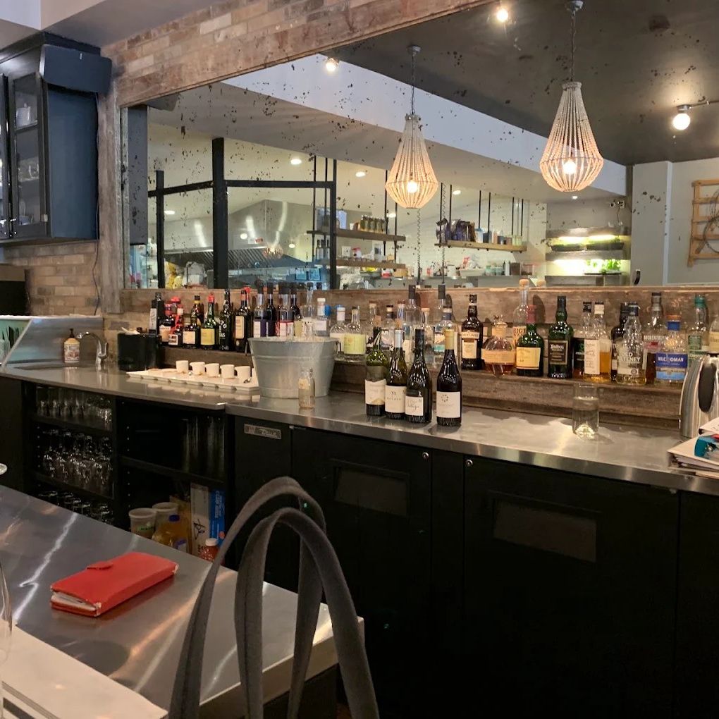 The bar at Fence & Post, with wine bottles on reclaimed wood and pendant lights