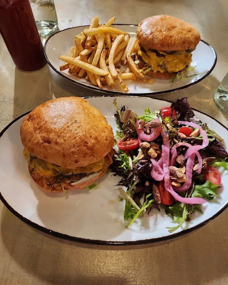 Two burgers on house buns, one with fries and one with a green salad and pickled onions