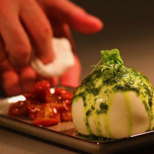 Burrata dressed in green herb oil beside roasted tomatoes