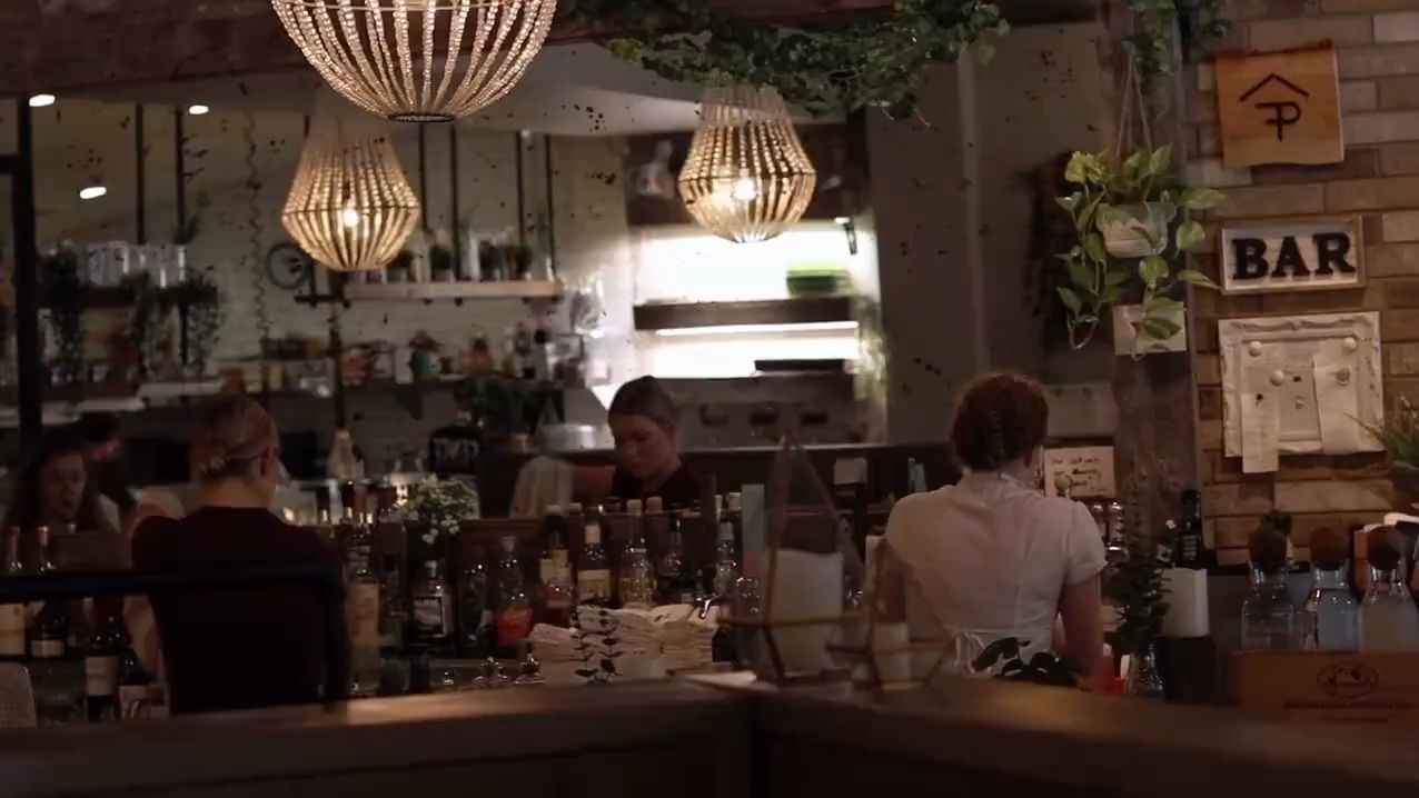 The bar at Fence & Post at night, under woven pendant lights, with staff at work and guests at the counter